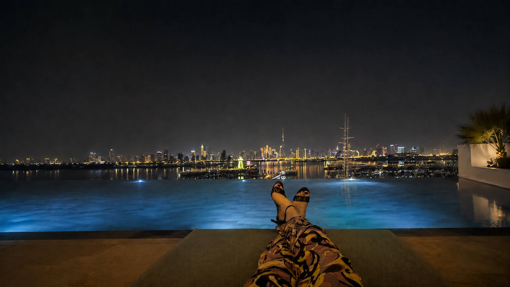 Blick vom Liegestuhl am Infinity-Pool auf eine nächtliche Skyline