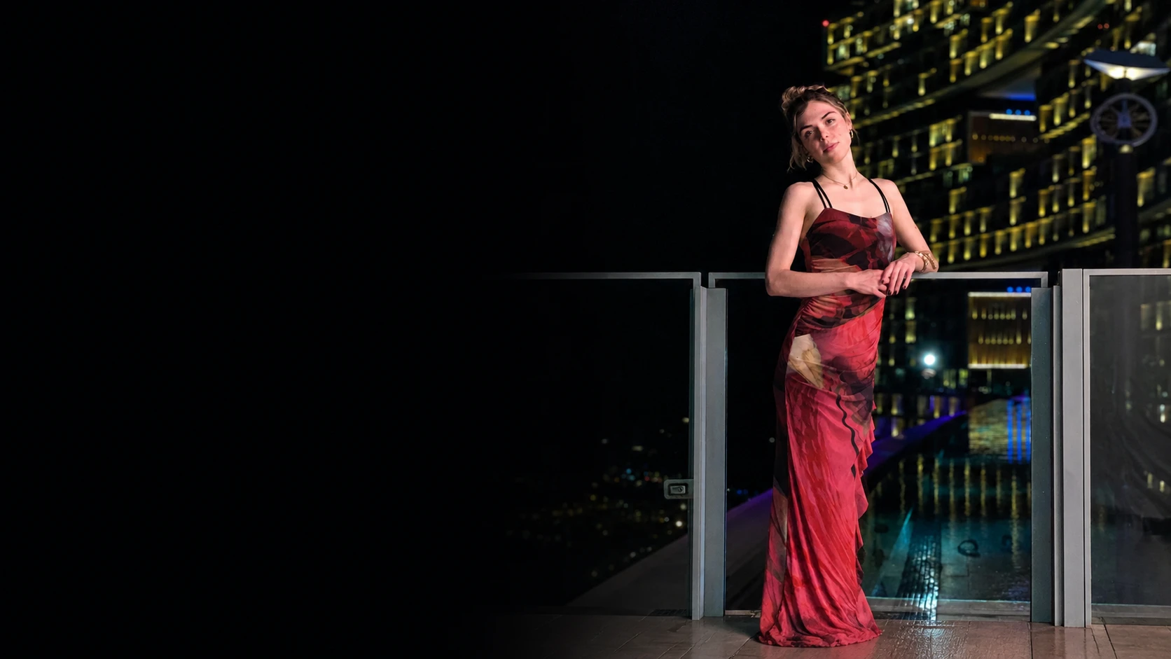 Olivia im roten Kleid auf einer Dachterrasse über der nächtlichen Stadt